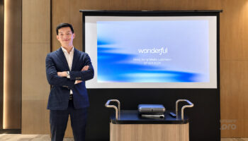 商務專業人士在演講廳前自信站立,背景為投影幕與企業簡報.